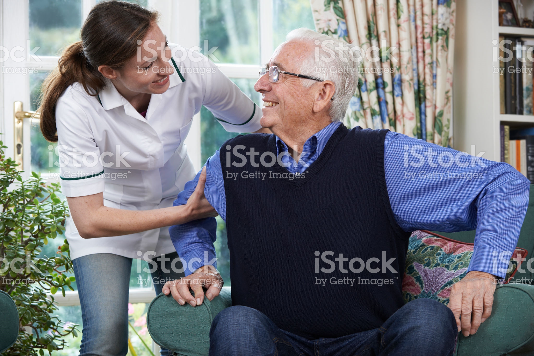 Care Worker Helping Senior Man To Get Up Out Of Chair